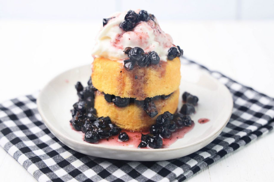 The Blueberry Shortcake comes on a white plate with a plaid napkin on a white wood backdrop.