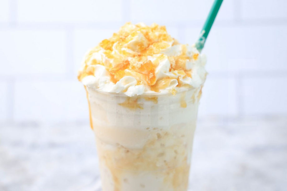 The Caramel Ribbon Crunch Crème Frappuccino comes in a venti cup with a white striped napkin on a marble backdrop.