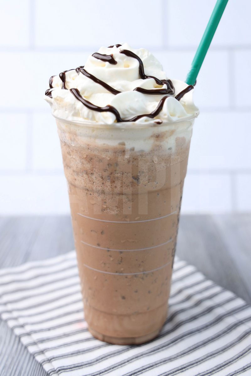 The Double Chocolaty Chip Crème Frappuccino comes in a venti cup with a white striped napkin on a gray wood backdrop.