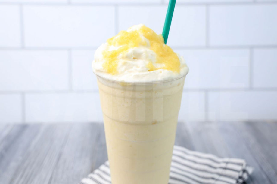 The Dole Whip Crème Frappuccino comes in a venti cup with a white striped napkin on a gray wood backdrop.