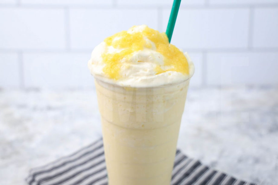 The Dole Whip Crème Frappuccino comes in a venti cup with a gray striped napkin on a marble backdrop.