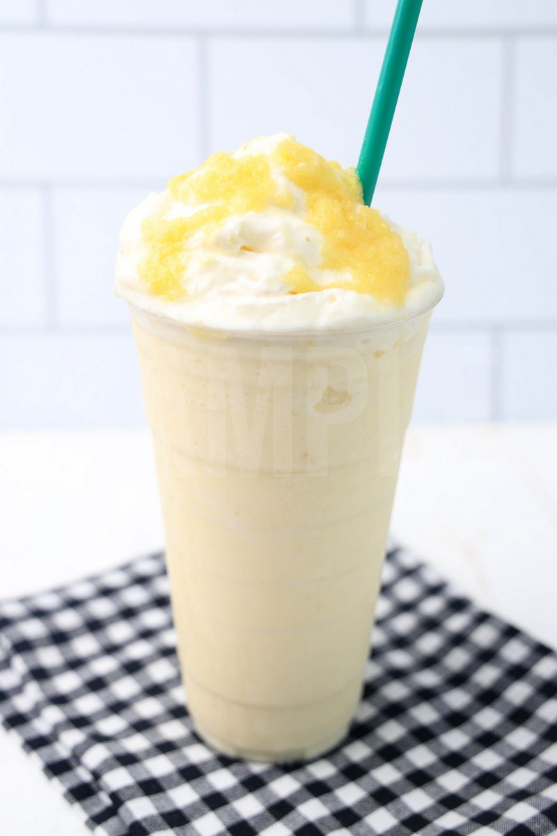 The Dole Whip Crème Frappuccino comes in a venti cup with a plaid napkin on a white wood backdrop.