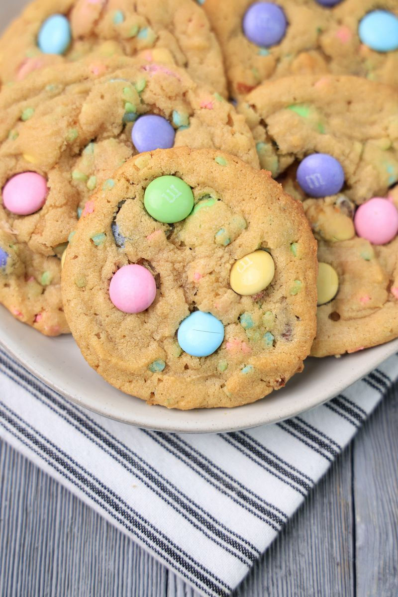 The Easter M&M Sprinkle Cookies comes on a white plate with a white striped napkin on a gray wood backdrop.