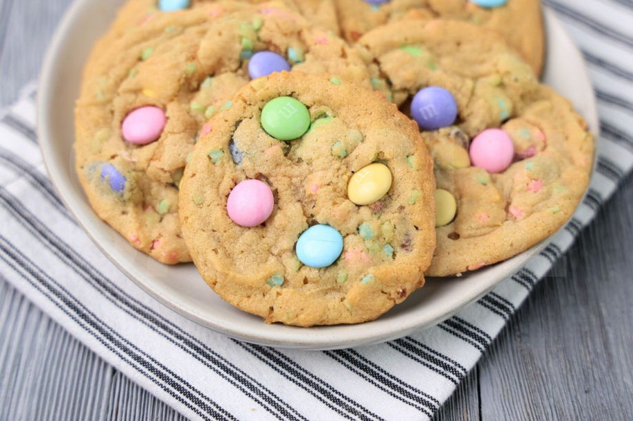 The Easter M&M Sprinkle Cookies comes on a white plate with a white striped napkin on a gray wood backdrop.