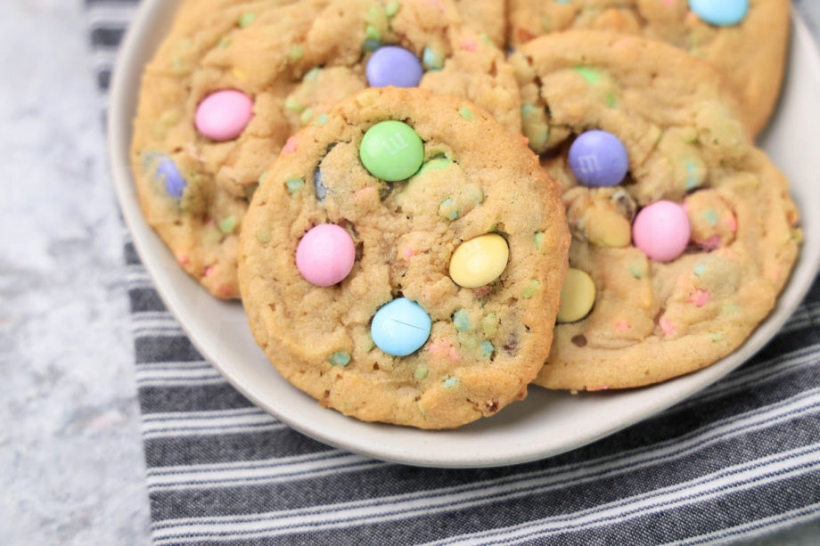 The Easter M&M Sprinkle Cookies comes on a white plate with a gray striped napkin on a marble backdrop.