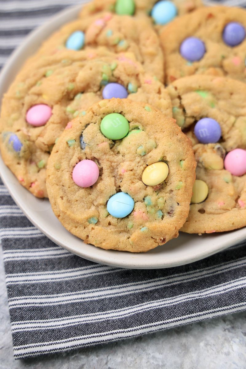 The Easter M&M Sprinkle Cookies comes on a white plate with a gray striped napkin on a marble backdrop.