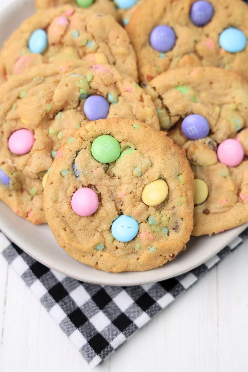 The Easter M&M Sprinkle Cookies comes on a white plate with a plaid napkin on a white wood backdrop.