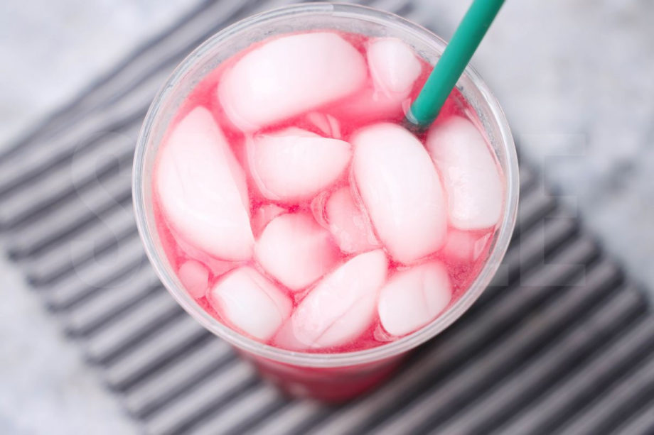 The Mango Dragonfruit Refresher comes in a venti cup with a gray striped napkin on a marble backdrop.