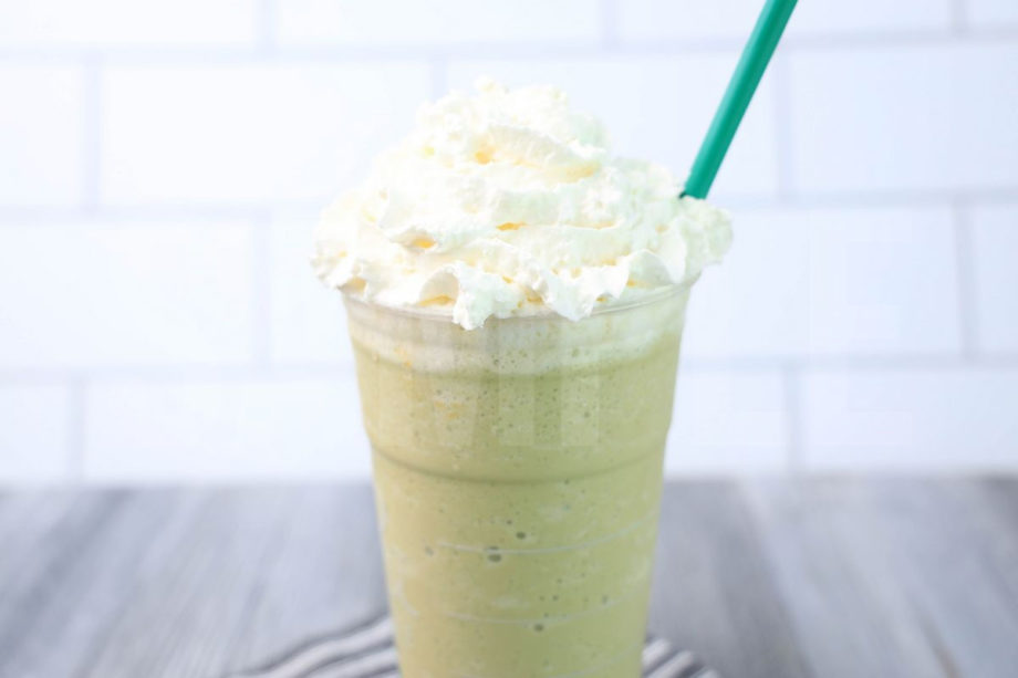 The Matcha Crème Frappuccino comes in a venti cup with a gray striped napkin on a gray wood backdrop.