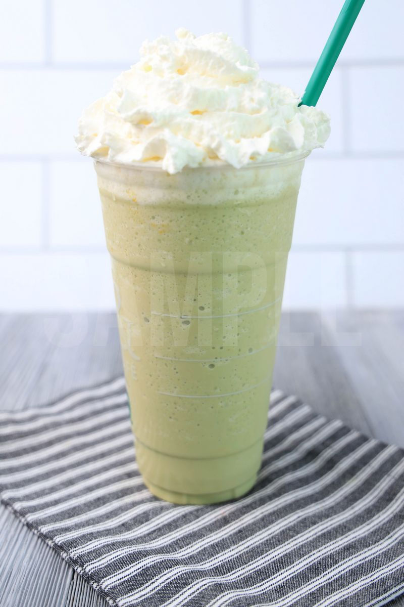 The Matcha Crème Frappuccino comes in a venti cup with a gray striped napkin on a gray wood backdrop.