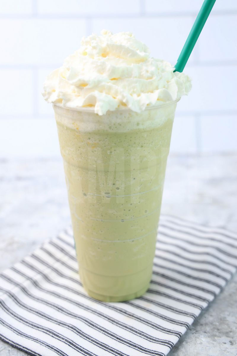The Matcha Crème Frappuccino comes in a venti cup with a white striped napkin on a marble backdrop.