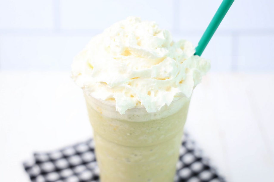 The Matcha Crème Frappuccino comes in a venti cup with a plaid napkin on a white wood backdrop.