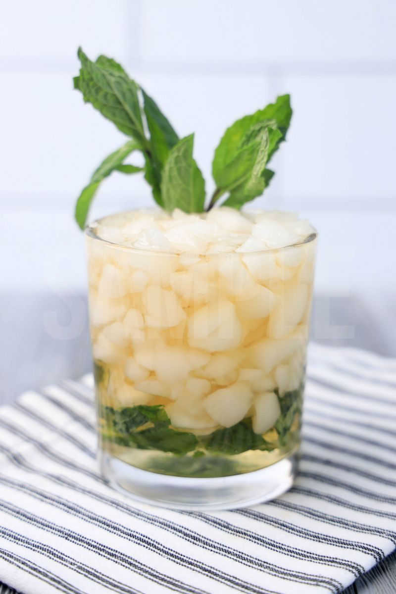 The Mint Julep comes in a glass with a white striped napkin on a gray wood backdrop.