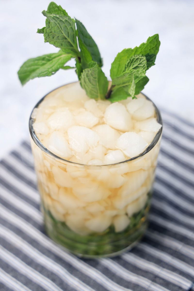 The Mint Julep comes in a glass with a gray striped napkin on a marble backdrop.