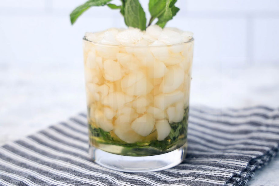 The Mint Julep comes in a glass with a gray striped napkin on a marble backdrop.