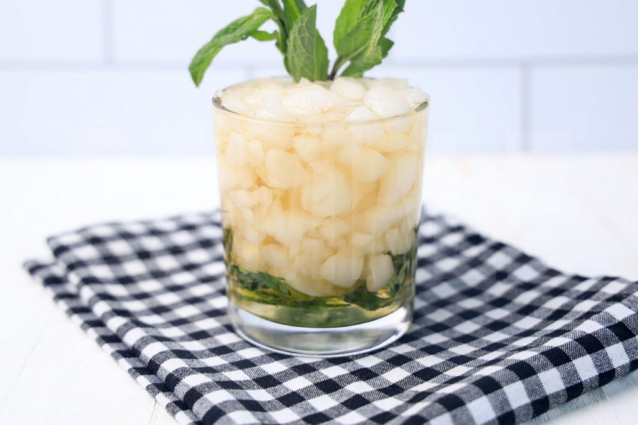The Mint Julep comes in a glass with a plaid napkin on a white wood backdrop.