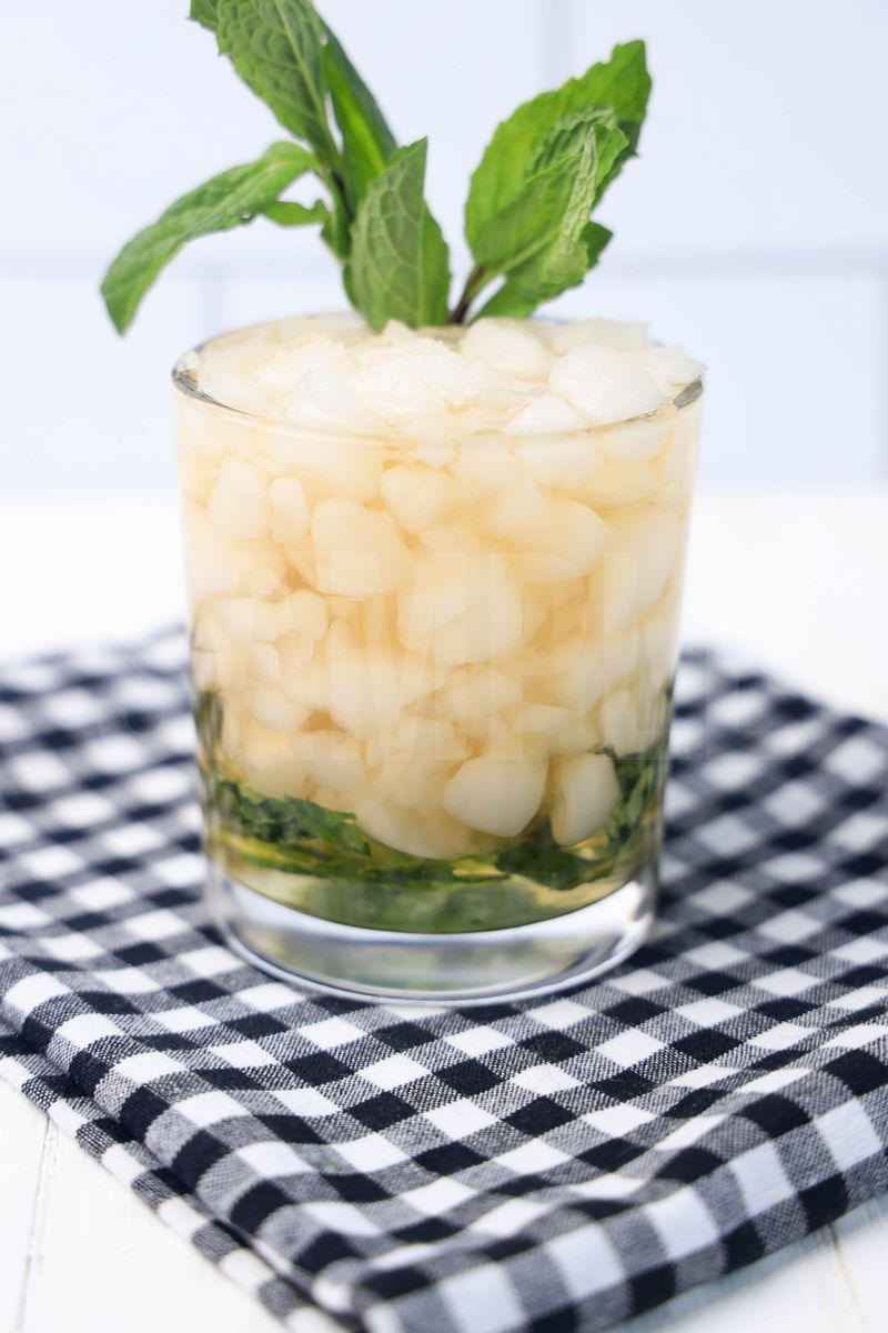 The Mint Julep comes in a glass with a plaid napkin on a white wood backdrop.