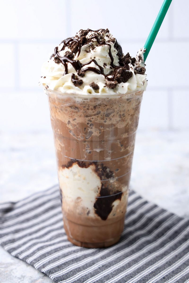 The Mocha Cookie Crumble Frappuccino comes in a venti cup with a gray striped napkin on a marble backdrop.