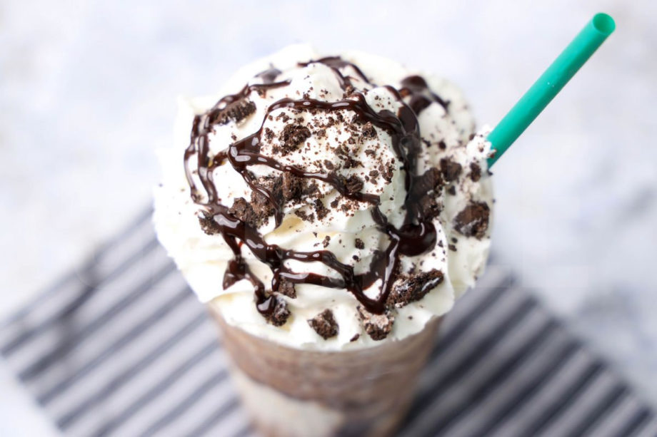 The Mocha Cookie Crumble Frappuccino comes in a venti cup with a gray striped napkin on a marble backdrop.