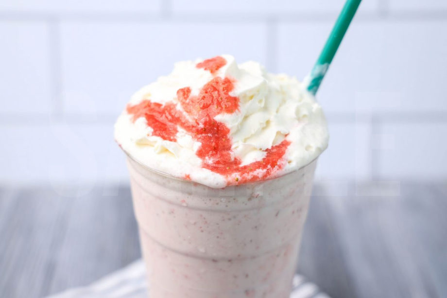 The Strawberry Crème Frappuccino comes in a venti cup with a white striped napkin on a gray wood backdrop.