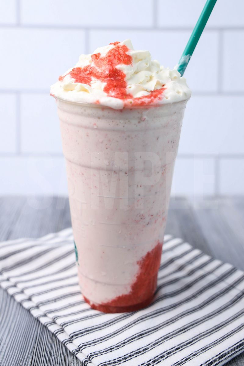 The Strawberry Crème Frappuccino comes in a venti cup with a white striped napkin on a gray wood backdrop.