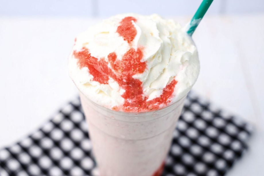The Strawberry Crème Frappuccino comes in a venti cup with a plaid napkin on a white wood backdrop.
