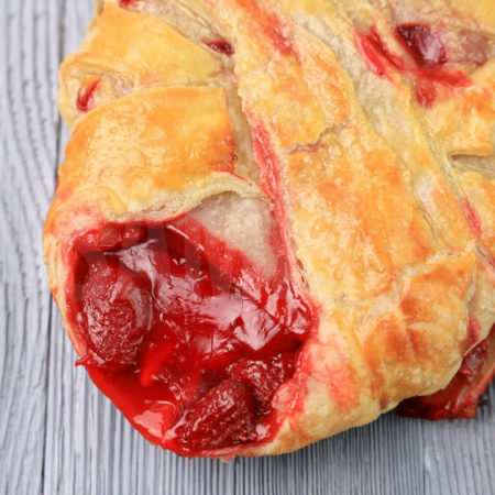 The Strawberry Puff Pastry Braid comes on a olive wood board on a gray wood backdrop.