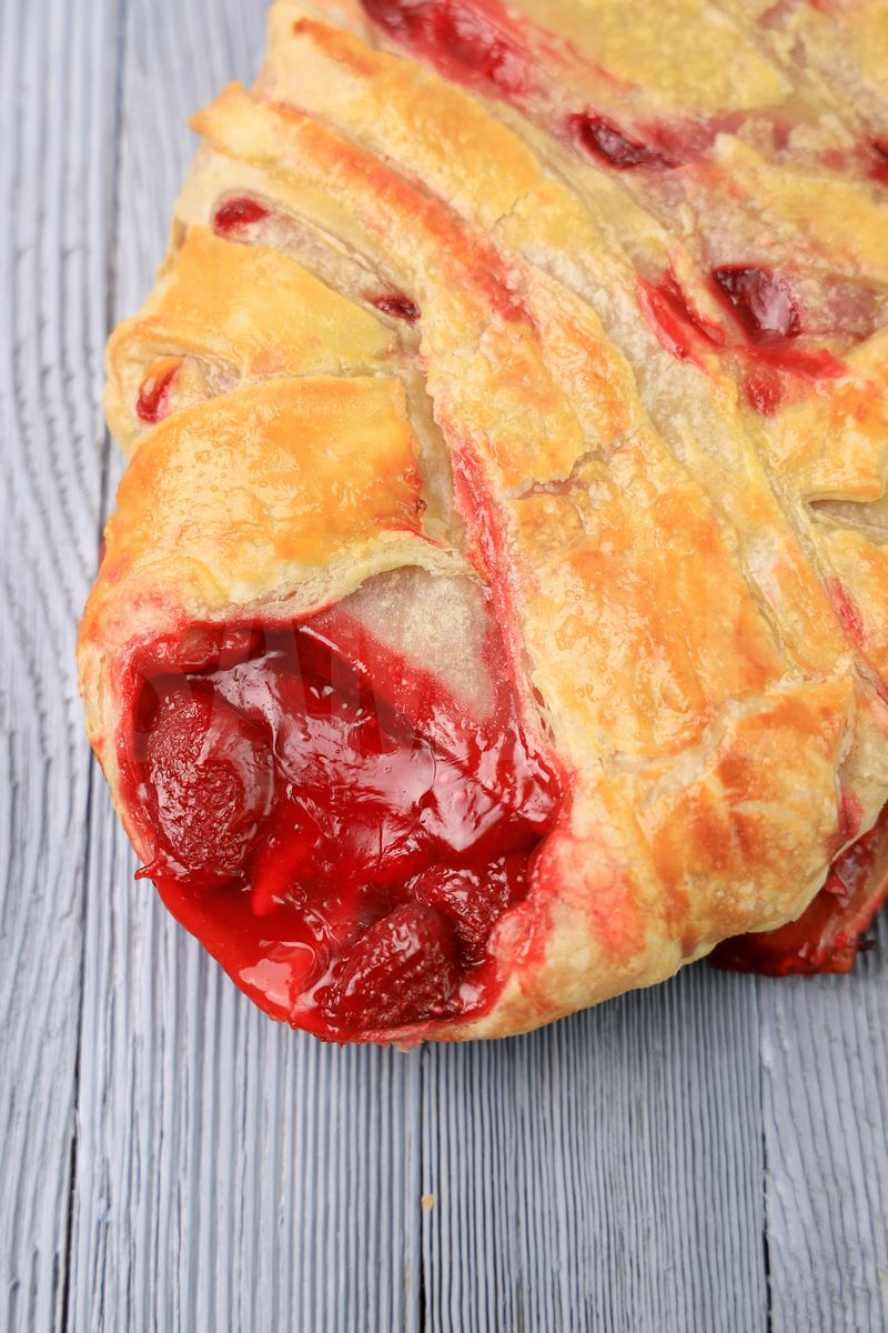The Strawberry Puff Pastry Braid comes on a olive wood board on a gray wood backdrop.