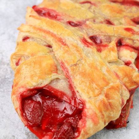 The Strawberry Puff Pastry Braid comes on a olive wood board on a marble backdrop.