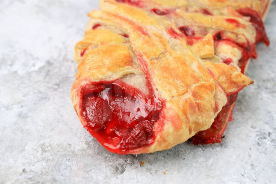 The Strawberry Puff Pastry Braid comes on a olive wood board on a marble backdrop.