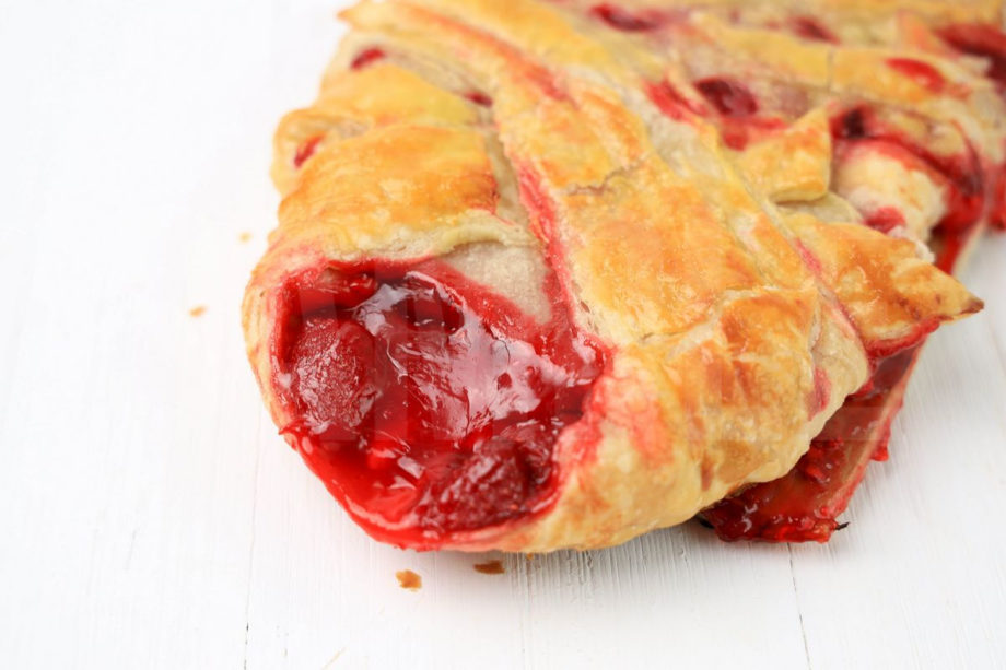 The Strawberry Puff Pastry Braid comes on a olive wood board on a white wood backdrop.