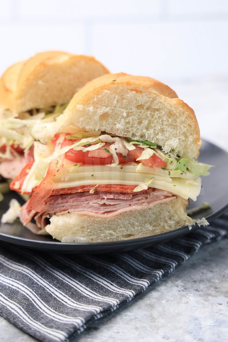 The Italian Grinder sandwich comes on a gray plaid with gray striped napkin on a marble backdrop.