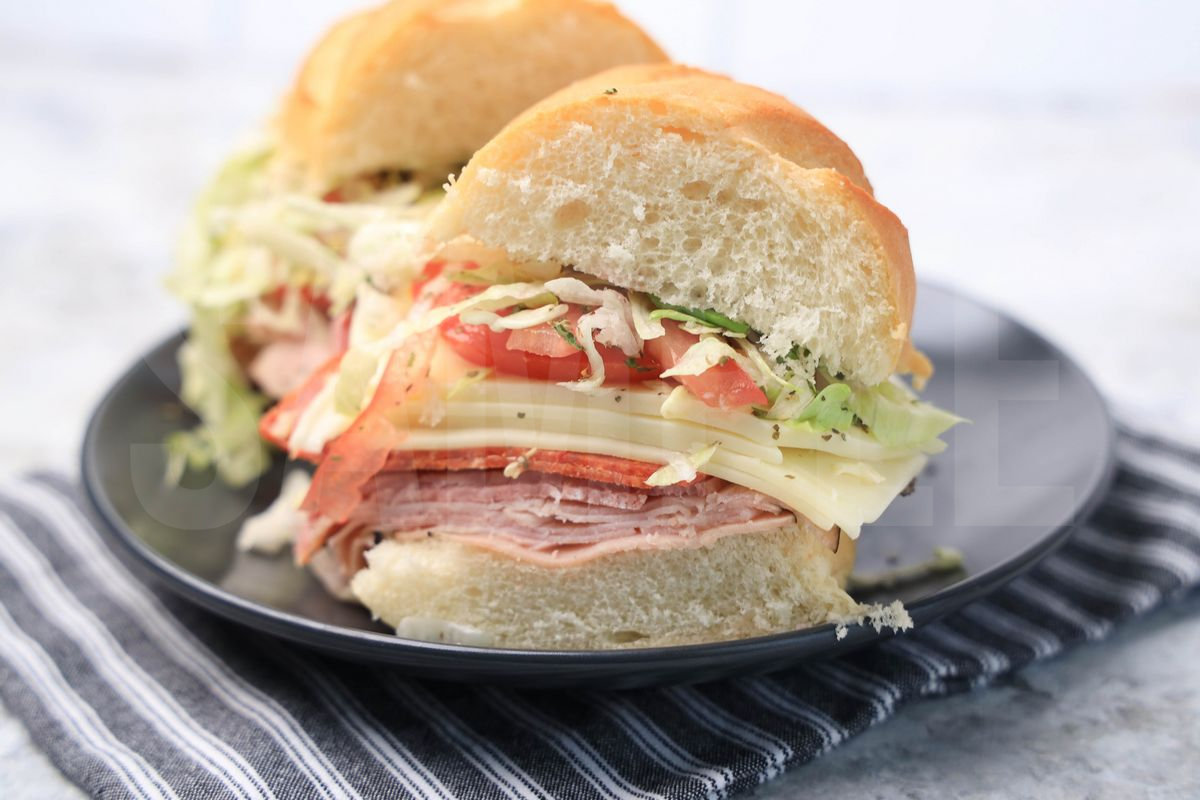 The Italian Grinder sandwich comes on a gray plaid with gray striped napkin on a marble backdrop.