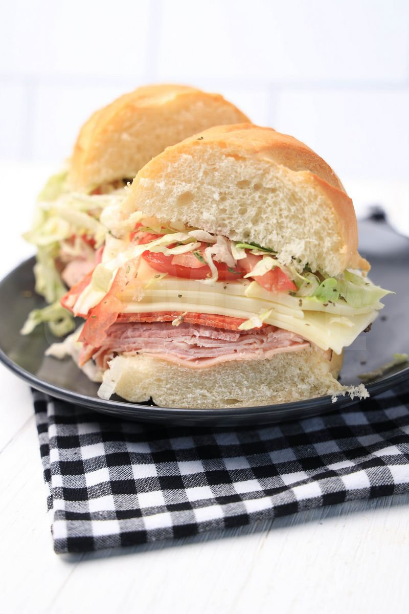 The Italian Grinder sandwich comes on a gray plate with plaid napkin on a white wood backdrop.