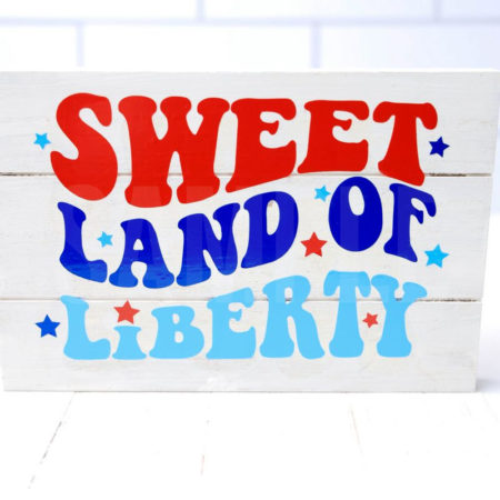 The Sweet Land Of Liberty Farmhouse Wood Cricut Craft comes pictured on a white wood backdrop.