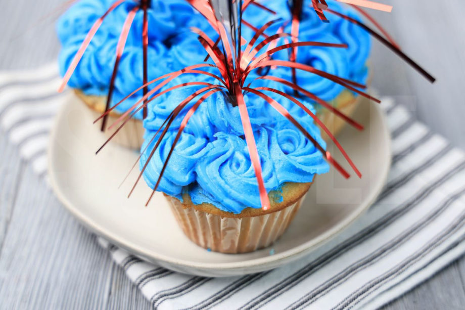 The 4th Of July Sparkler Cupcakes comes on a white striped napkin on a gray wood backdrop.