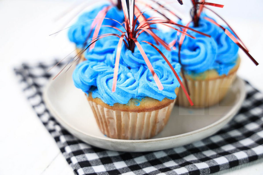 The 4th Of July Sparkler Cupcakes comes on a plaid napkin on a white wood backdrop.