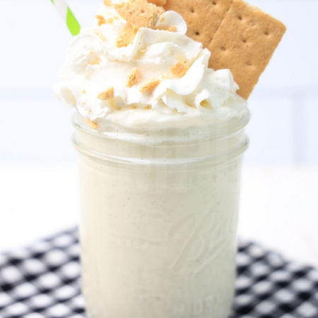 The Key Lime Pie Milkshake comes in a glass jar on a plaid napkin on a white wood backdrop.