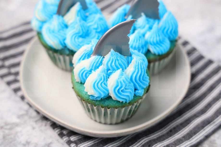 The Shark Cupcakes comes on a gray striped napkin on a marble backdrop.