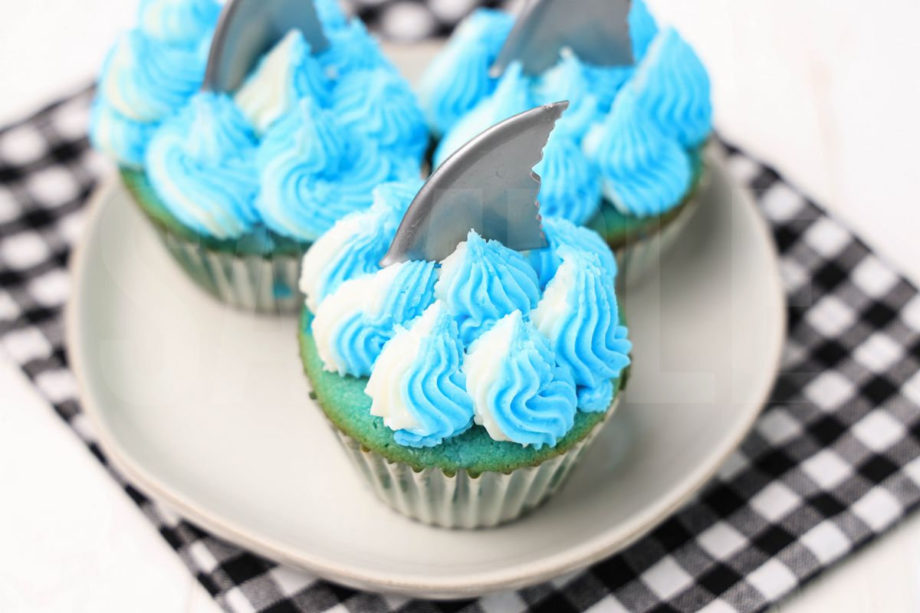 The Shark Cupcakes comes on a plaid napkin on a white wood backdrop.