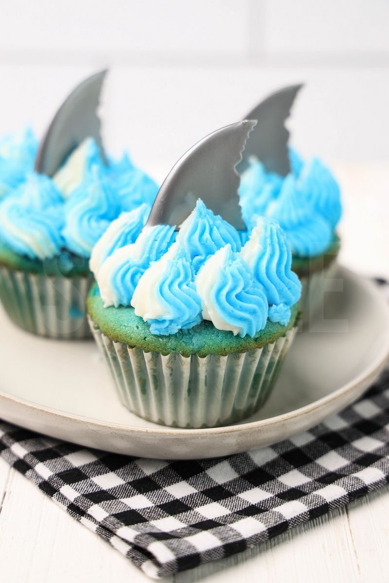 The Shark Cupcakes comes on a plaid napkin on a white wood backdrop.