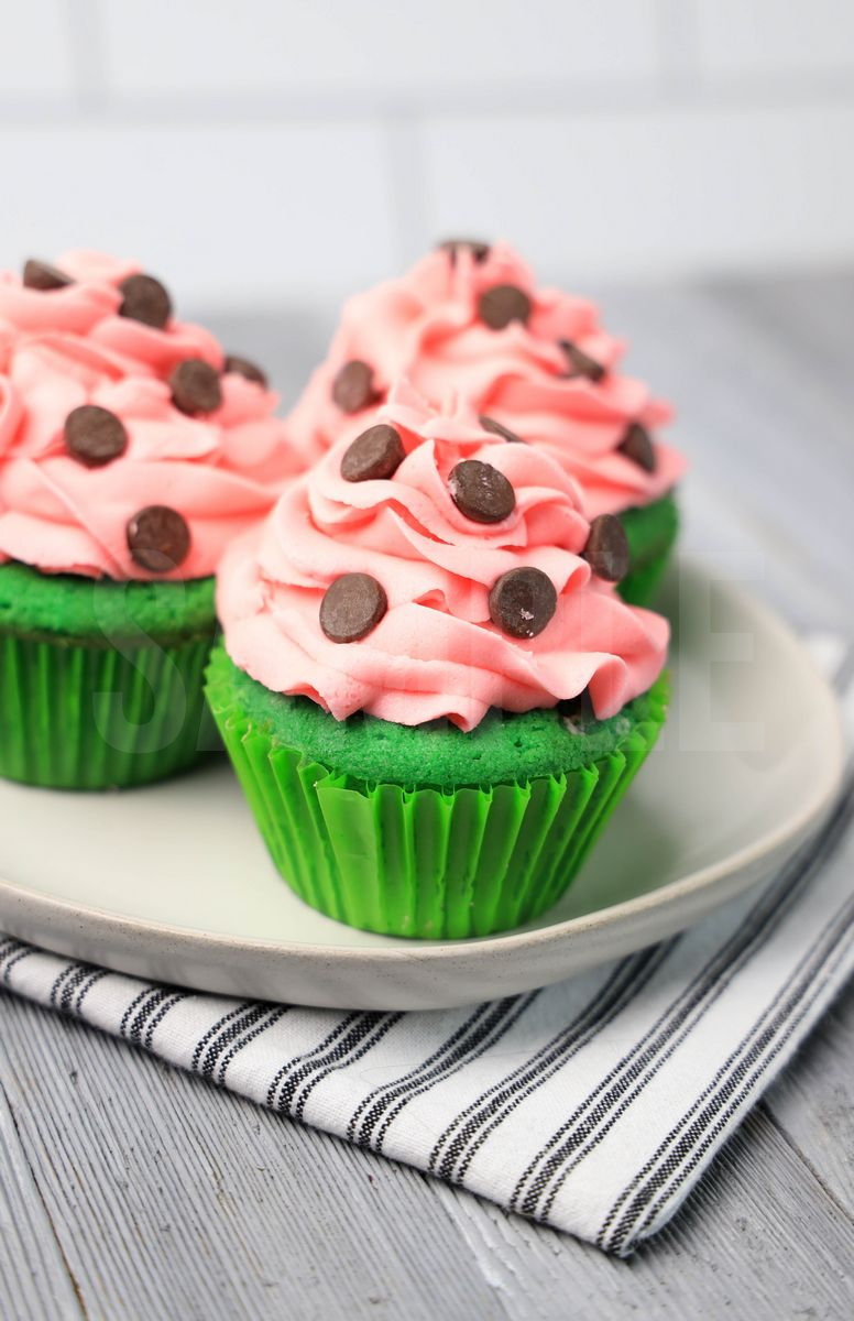 The Watermelon Cupcakes comes on a white plate with a white striped napkin on a gray wood backdrop.