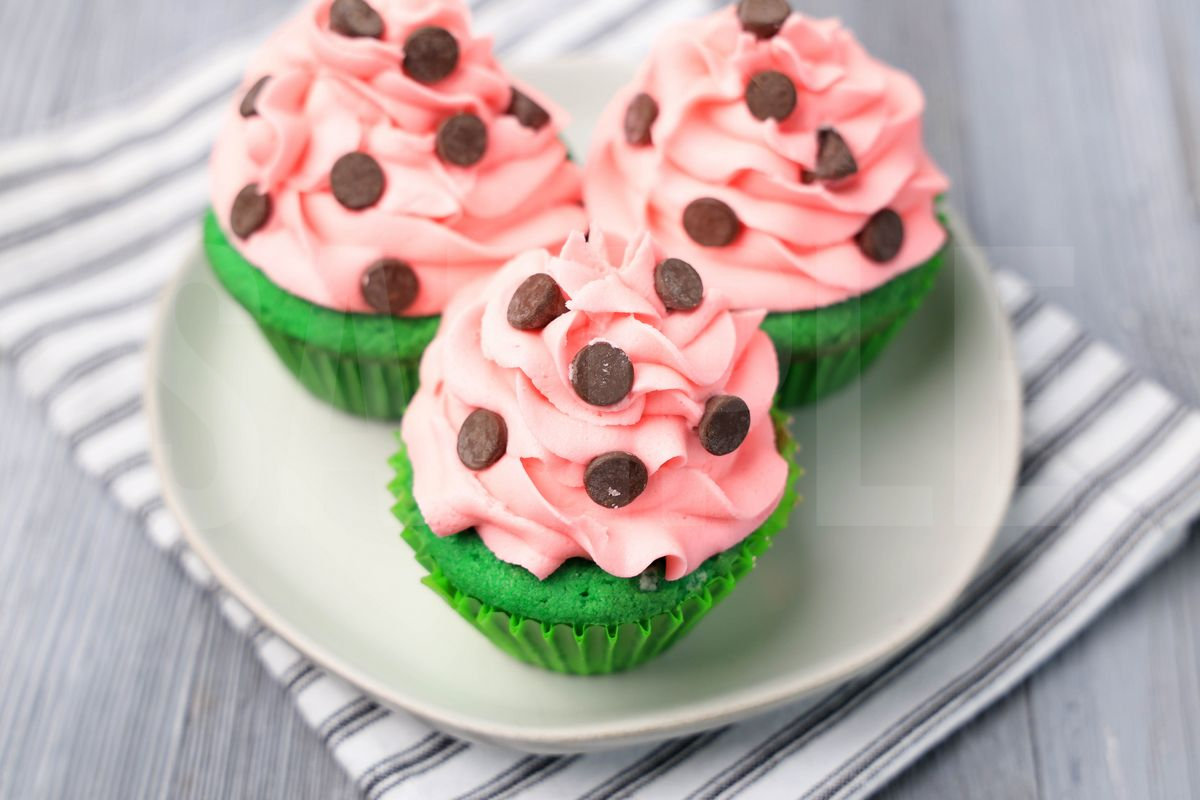 The Watermelon Cupcakes comes on a white plate with a white striped napkin on a gray wood backdrop.