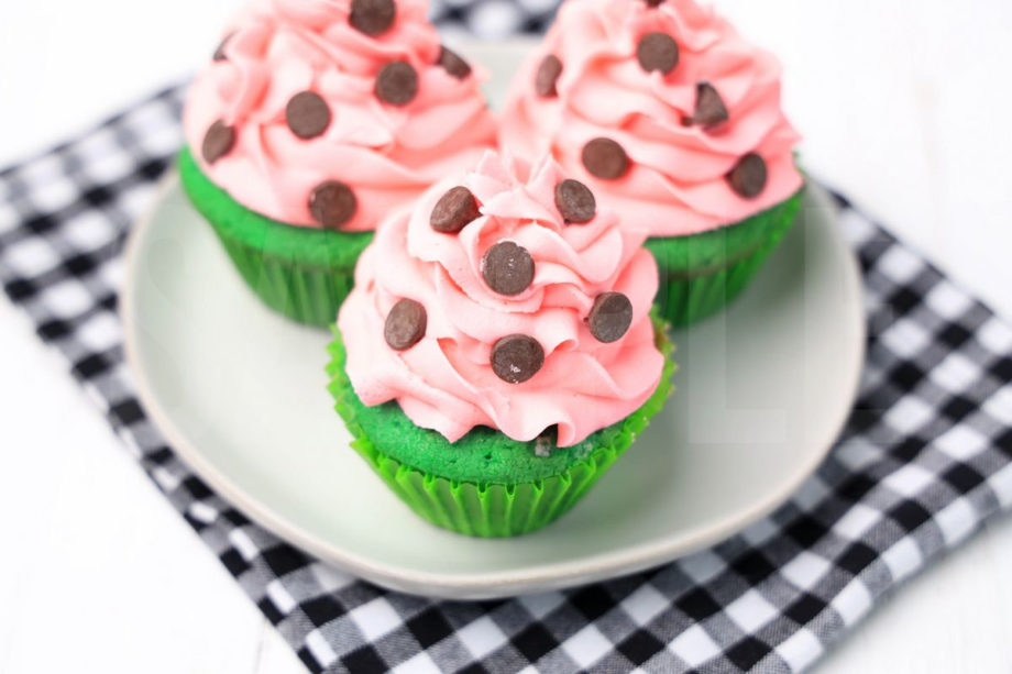 The Watermelon Cupcakes comes on a white plate with a plaid napkin on a white wood backdrop.