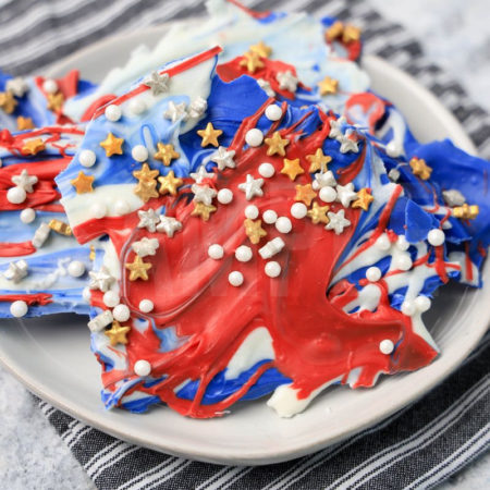 The 4th Of July Candy Bark comes on a white plate with a gray striped napkin on a marble backdrop.