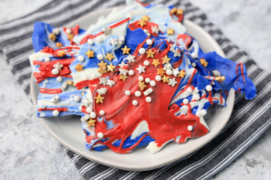 The 4th Of July Candy Bark comes on a white plate with a gray striped napkin on a marble backdrop.