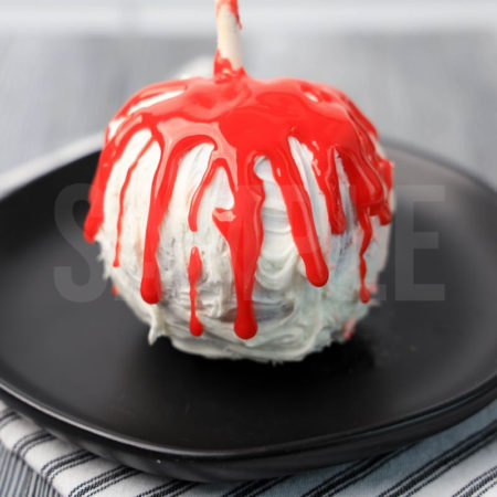 The Bloody Candy Apples comes on a black plate with a white striped napkin on a gray wood backdrop.