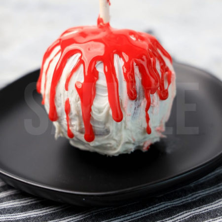 The Bloody Candy Apples comes on a black plate with a gray striped napkin on a marble backdrop.