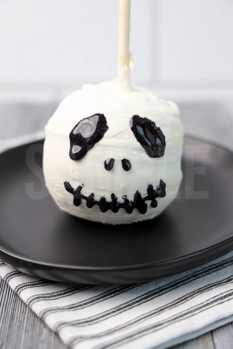 The Jack Skellington Candy Apples comes on a black plate with a white striped napkin on a gray wood backdrop.