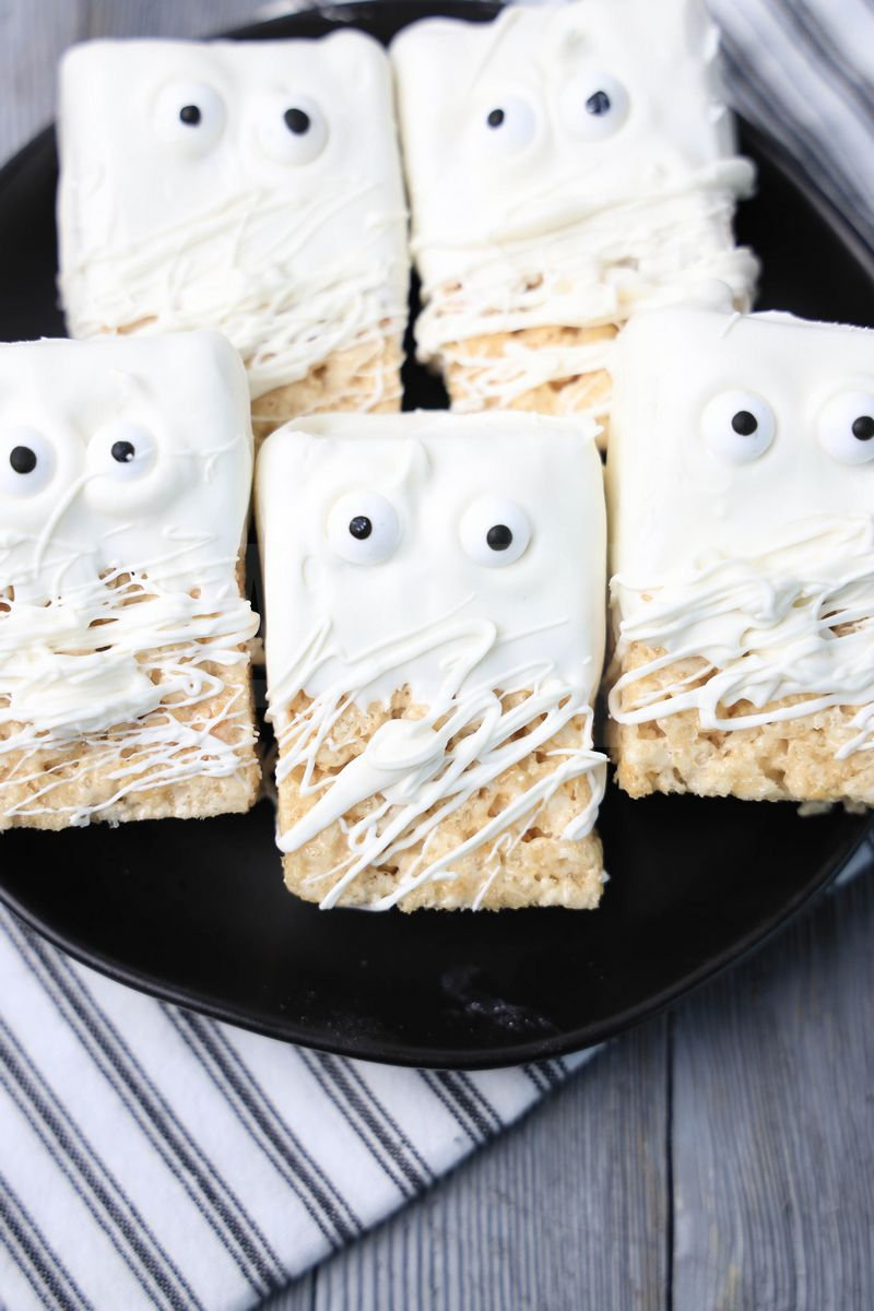 The Mummy Rice Krispy Treats comes on a black plate with a white striped napkin on a gray wood backdrop.